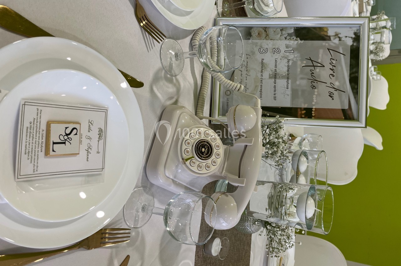 Table décorée pour un événement avec assiettes, verres, téléphone rétro et cadre contenant des instructions.