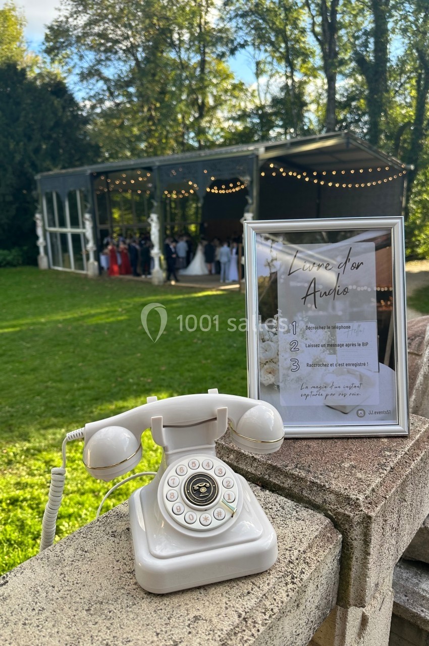Téléphone rétro blanc et cadre explicatif posés sur un muret, avec une réception en plein air en arrière-plan.