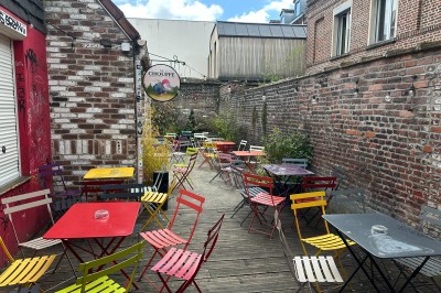 Terrasse extérieure avec tables et chaises colorées, entourée de murs en briques et végétation.