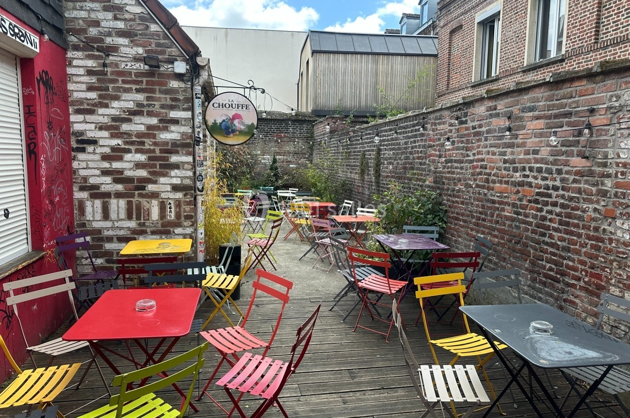 Terrasse extérieure avec tables et chaises colorées, entourée de murs en briques et végétation.