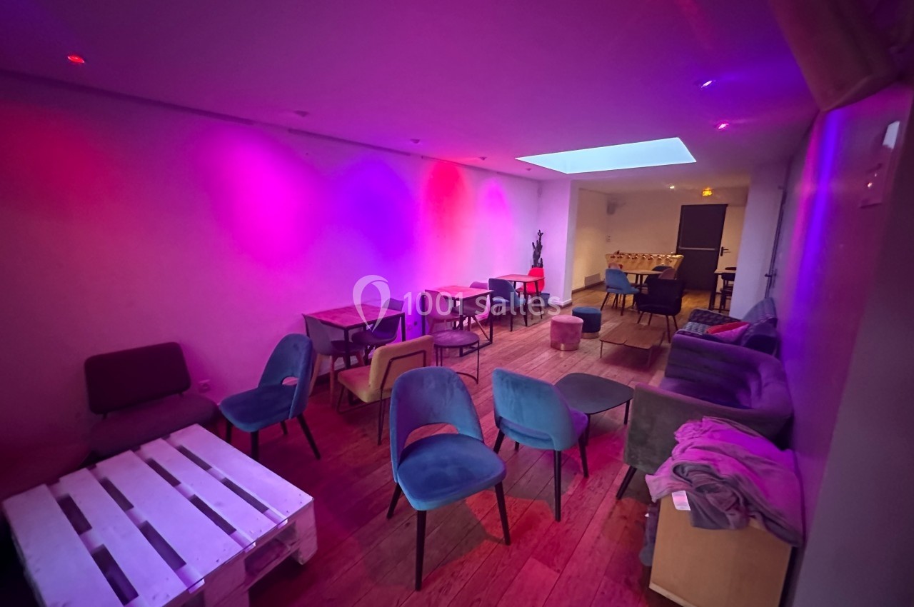 Salle lumineuse avec des chaises colorées, des tables en bois et un éclairage tamisé aux tons violets et roses.