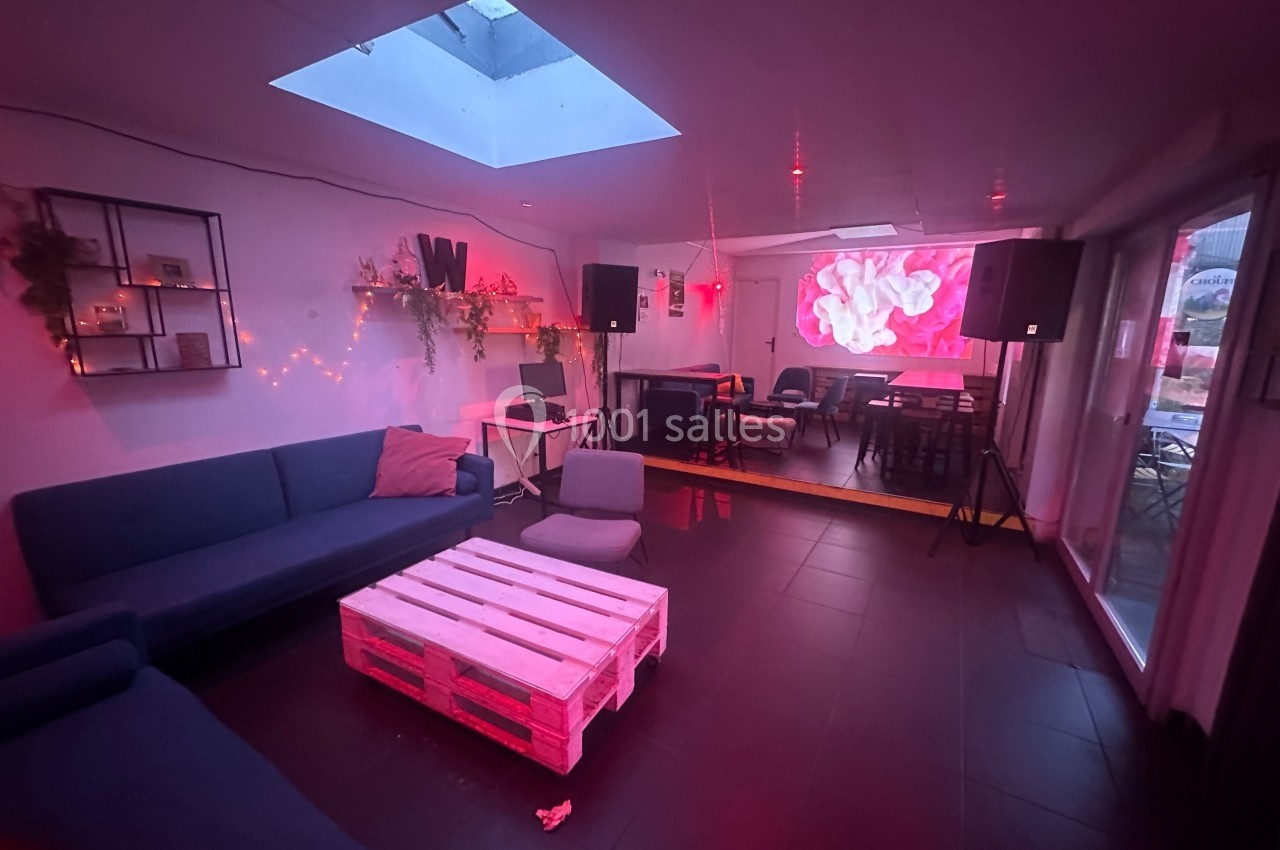 Salle moderne avec canapé, table basse en palettes, éclairage rouge, écran mural et grandes baies vitrées.