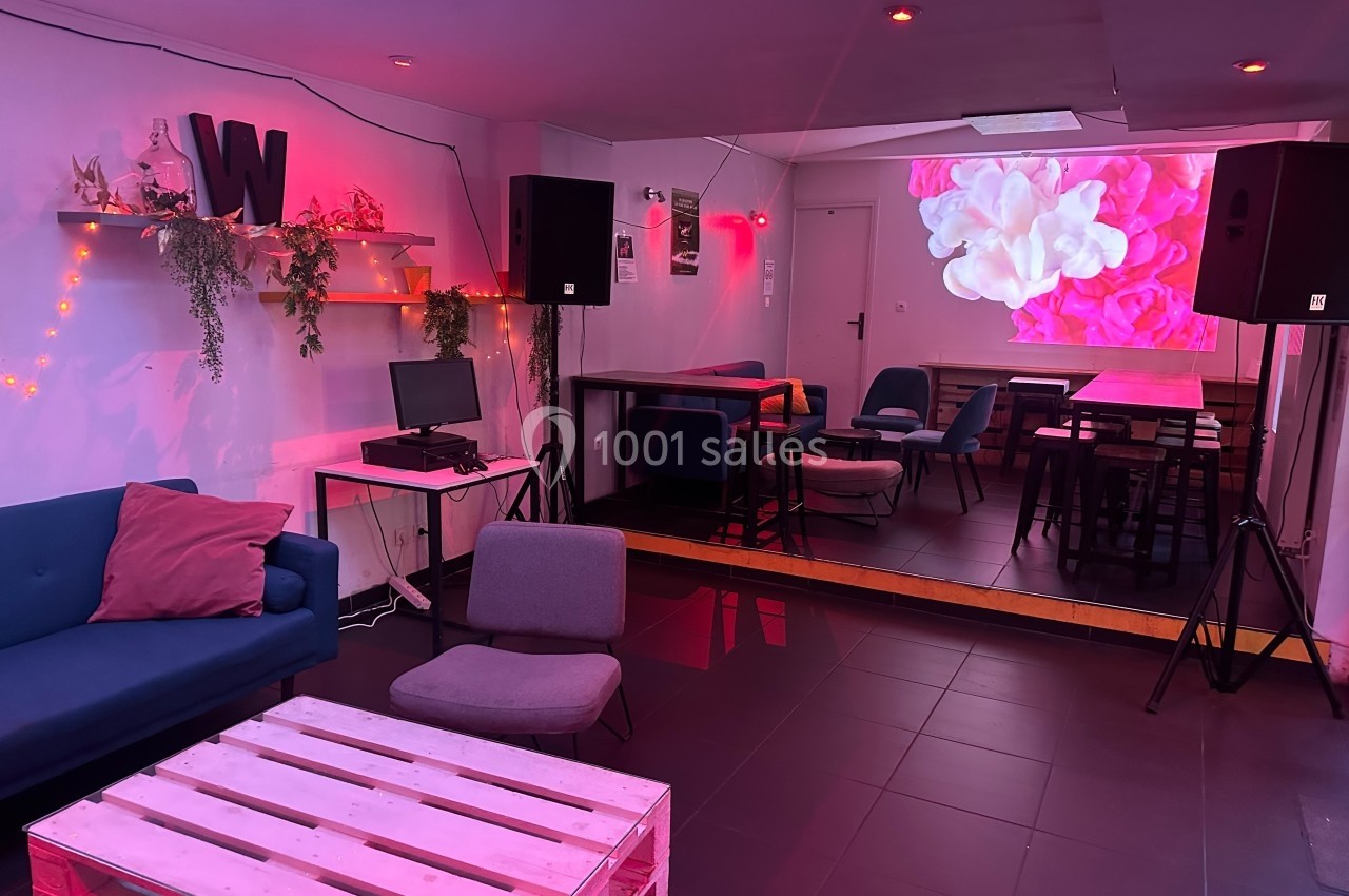 Salle moderne avec éclairage rose, canapé, tables, chaises, étagères décorées et écran projetant des fleurs.