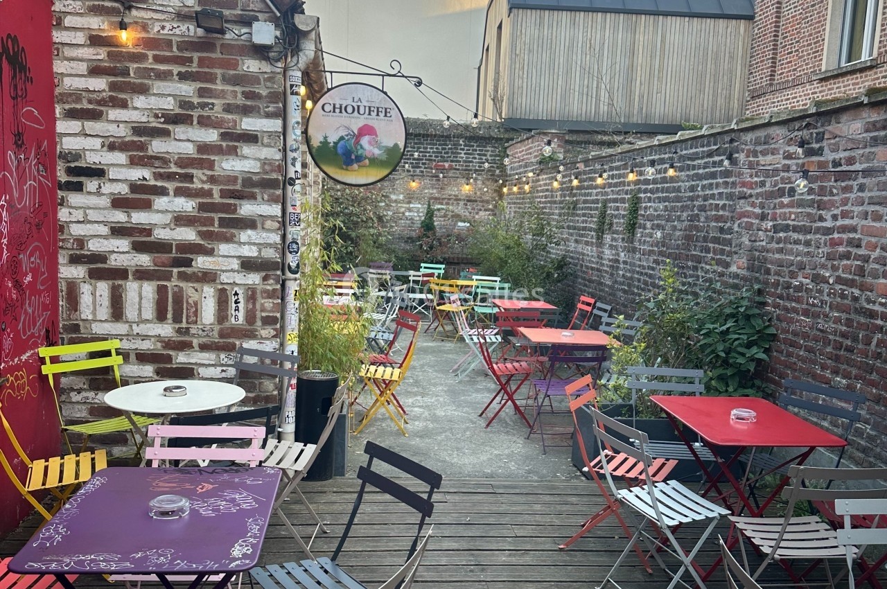 Terrasse extérieure avec tables et chaises colorées, entourée de murs en briques et décorée de guirlandes lumineuses.