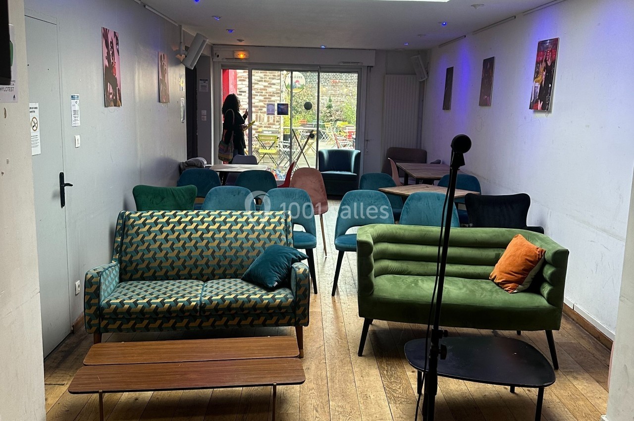 Salle avec des fauteuils et des chaises disposés face à une scène, éclairée par la lumière naturelle d'une baie vitrée.