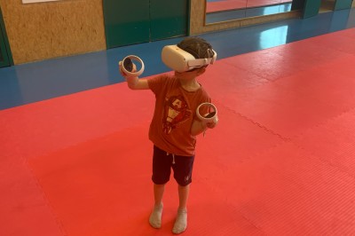 Homme portant un casque de réalité virtuelle et tenant deux manettes dans une pièce au sol en bois.