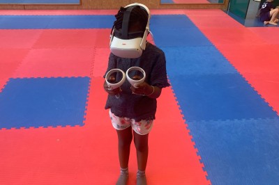 Homme portant un casque de réalité virtuelle et tenant deux manettes dans une pièce au sol en bois.