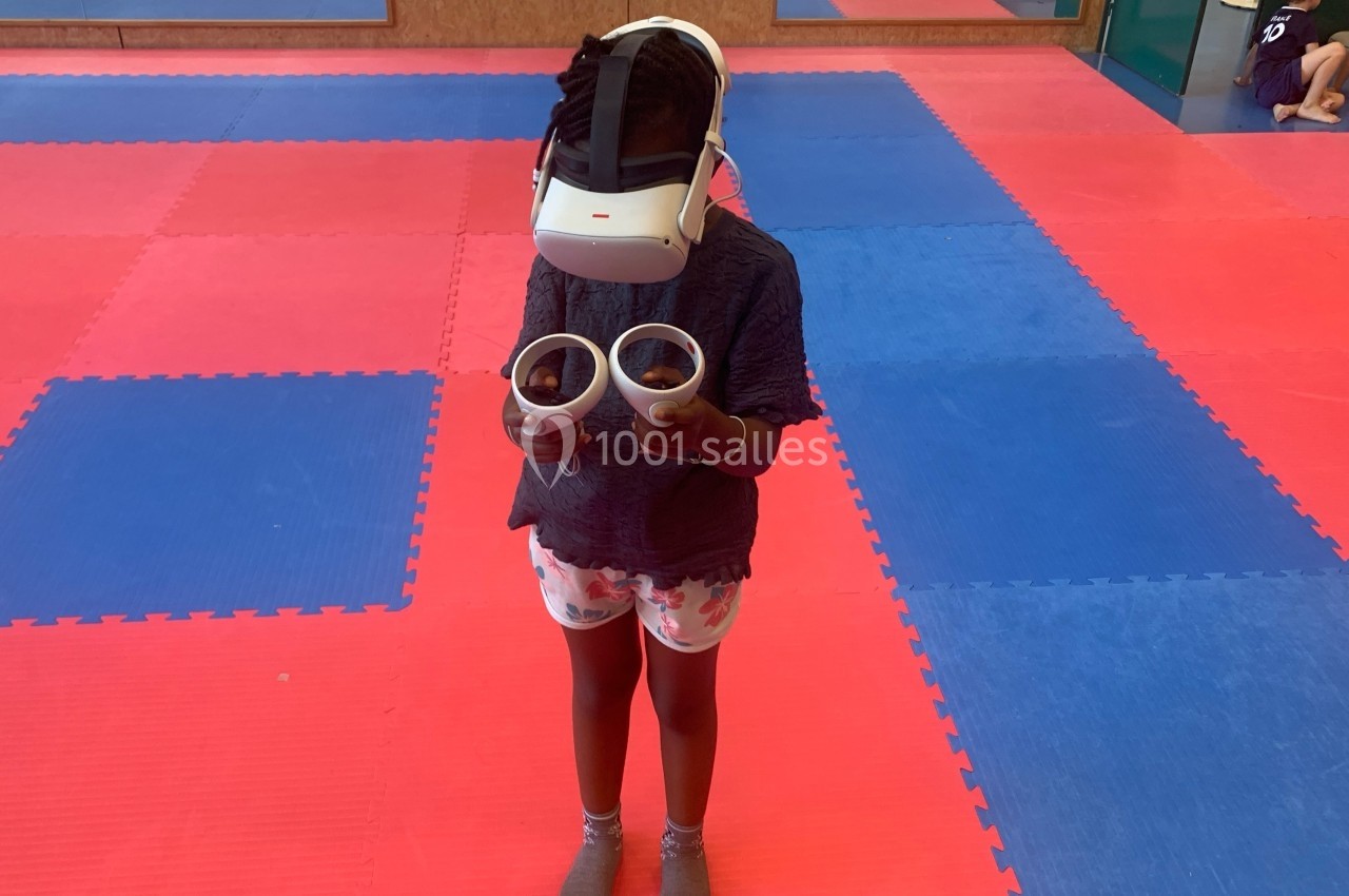 Enfant debout sur un sol en tapis colorés, portant un casque de réalité virtuelle et tenant des manettes.
