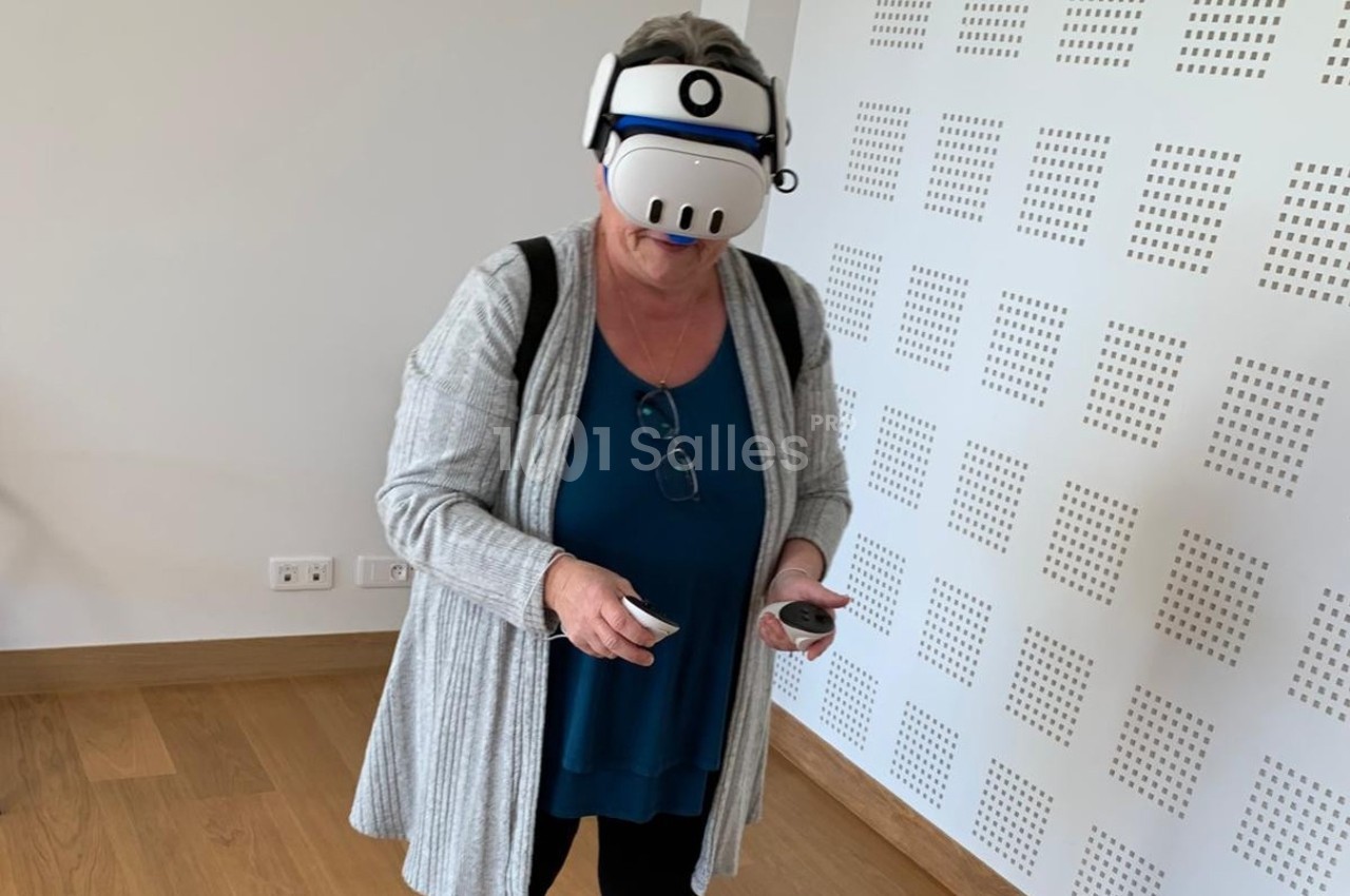 Femme portant un casque de réalité virtuelle dans une pièce lumineuse, tenant des contrôleurs dans les mains.
