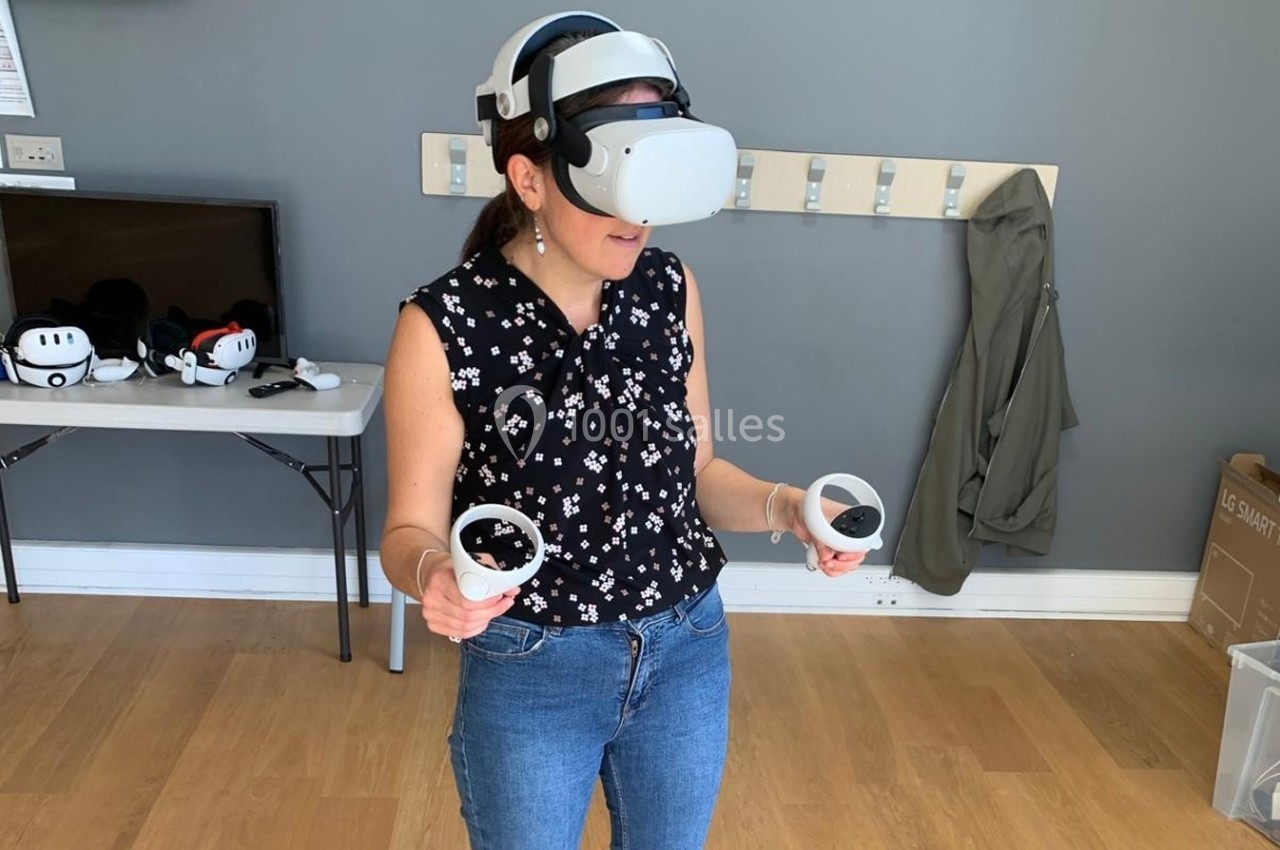 Femme utilisant un casque de réalité virtuelle avec des manettes dans une pièce au sol en bois.