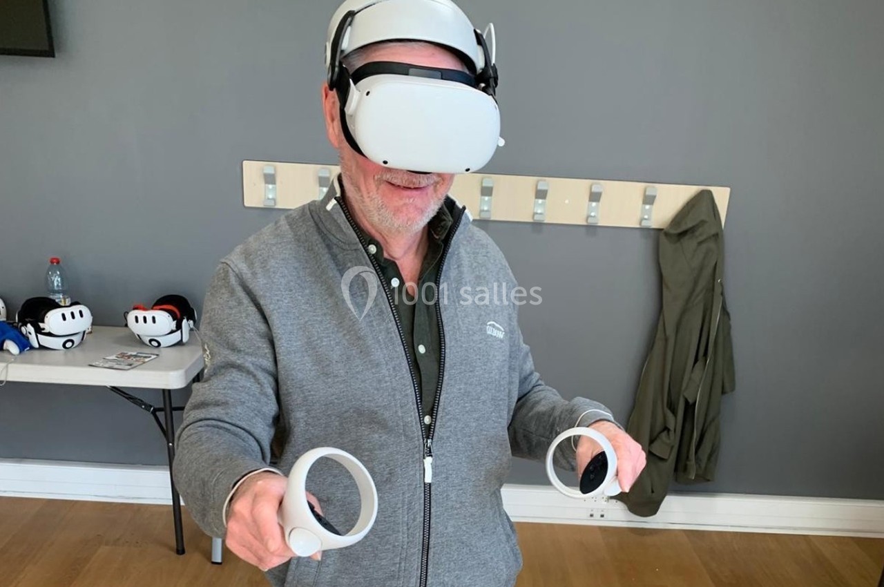 Un homme utilise un casque de réalité virtuelle avec des manettes dans une pièce équipée de crochets muraux.