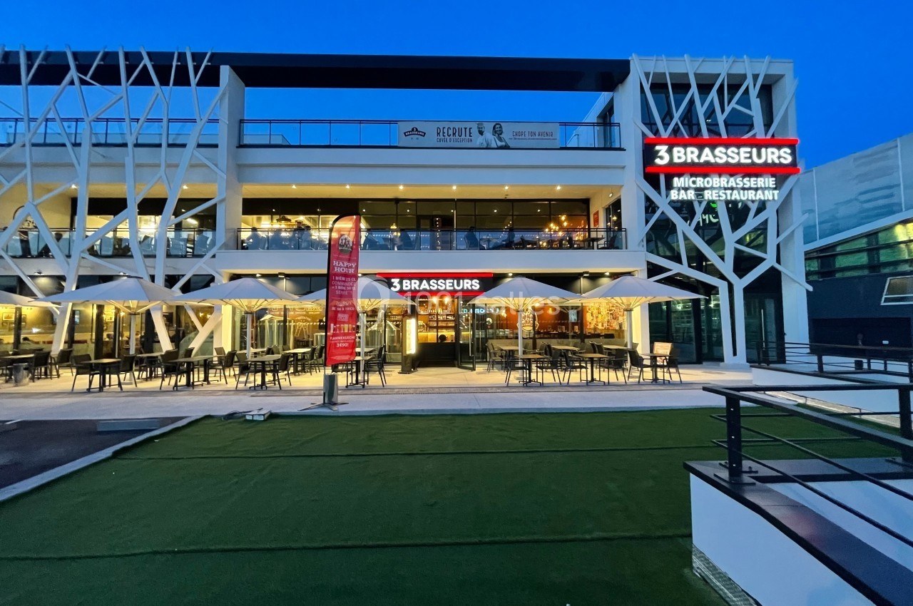 Façade éclairée d'un restaurant ’3 Brasseurs’ avec terrasse extérieure et enseignes lumineuses, en soirée.