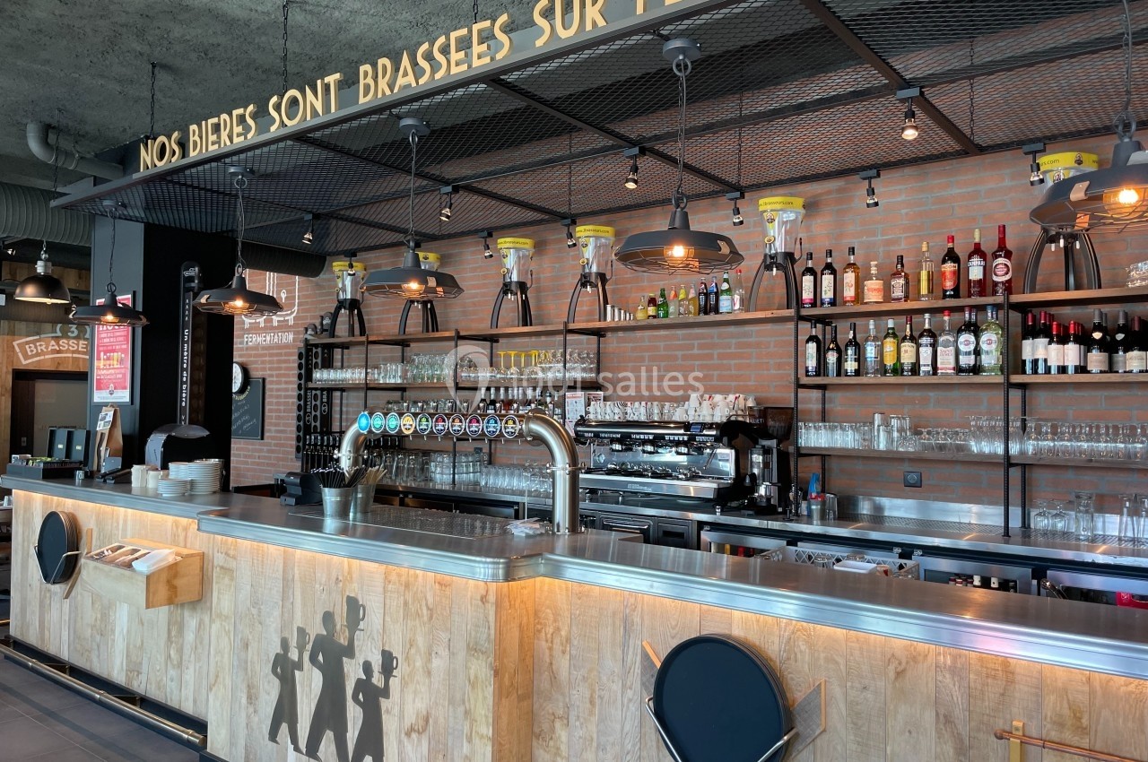Comptoir de bar moderne avec tireuses à bière, étagères de bouteilles et enseigne indiquant une brasserie sur place.