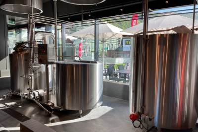 Miniature Location salle Étrembières (Haute-Savoie) - 3 Brasseurs #8 Cuves en acier inoxydable dans une brasserie artisanale, avec vue sur une terrasse extérieure ensoleillée.