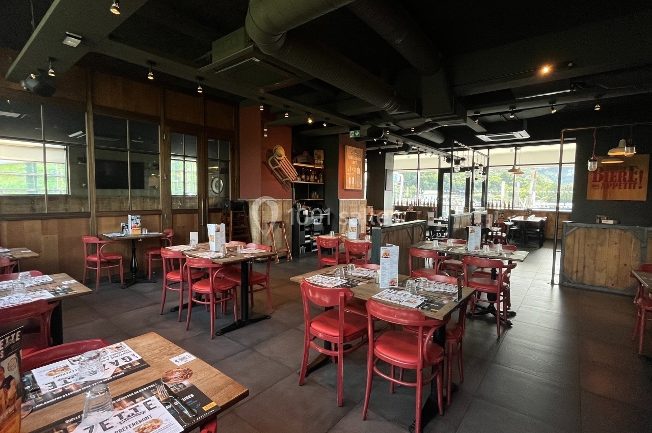 Salle de restaurant avec tables en bois, chaises rouges, décoration industrielle et lumière naturelle entrant par les…