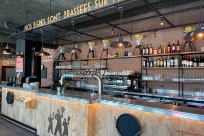 Salle de restaurant avec tables en bois, chaises rouges et noires, éclairage suspendu et grandes fenêtres donnant sur l…