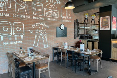 Salle de restaurant avec tables en bois, chaises rouges et noires, éclairage suspendu et grandes fenêtres donnant sur l…