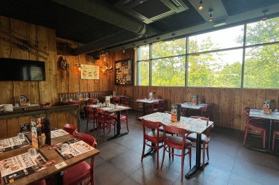 Salle de restaurant avec tables en bois, chaises rouges et noires, éclairage suspendu et grandes fenêtres donnant sur l…