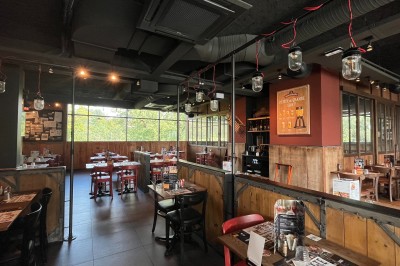 Salle de restaurant avec tables en bois, chaises rouges et noires, éclairage suspendu et grandes fenêtres donnant sur l…