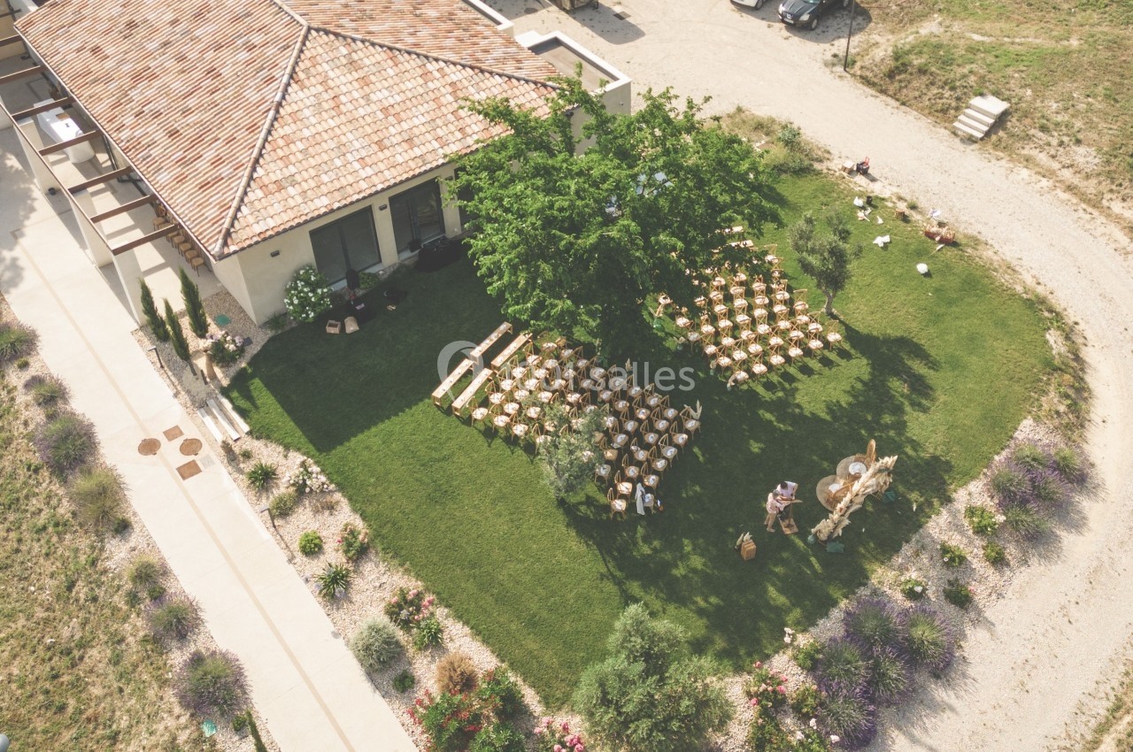 Vue aérienne d'un jardin avec des chaises disposées pour un événement, près d'une maison au toit en tuiles.