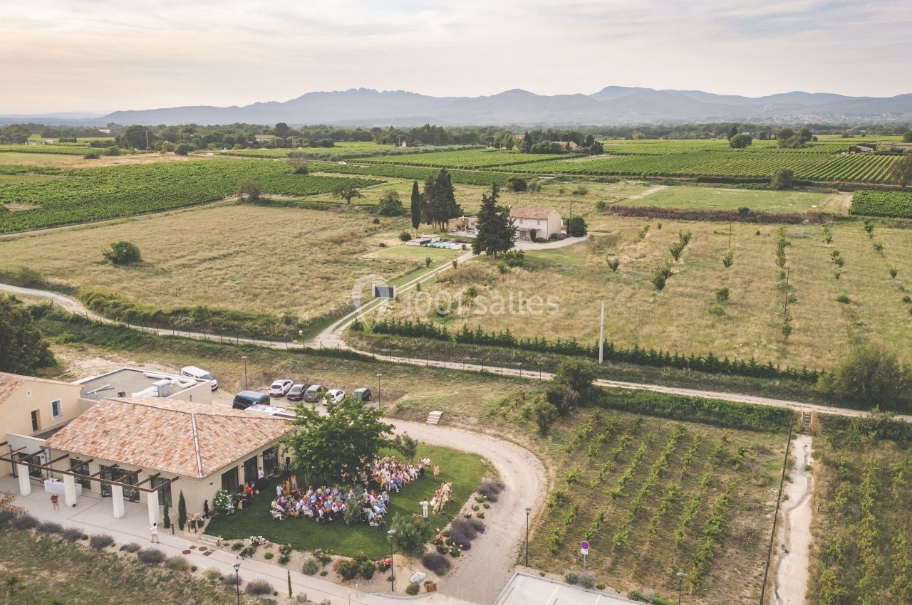 Vue aérienne d'une propriété rurale entourée de vignes et de champs, avec un groupe de personnes rassemblées à l'extérieur.
