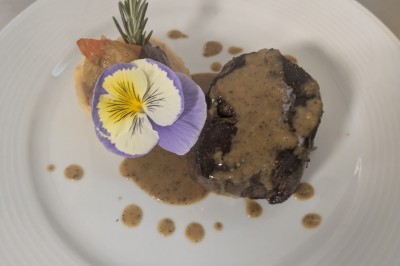 Bâtiment moderne éclairé en soirée, entouré d'arbres et d'un jardin sombre sous un ciel crépusculaire.