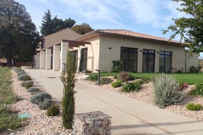 Bâtiment moderne éclairé en soirée, entouré d'arbres et d'un jardin sombre sous un ciel crépusculaire.
