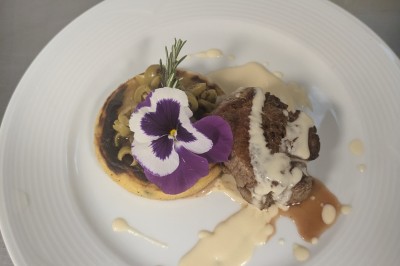 Assiette avec un morceau de viande nappé de sauce, purée, garniture de légumes et fleur comestible en décoration.