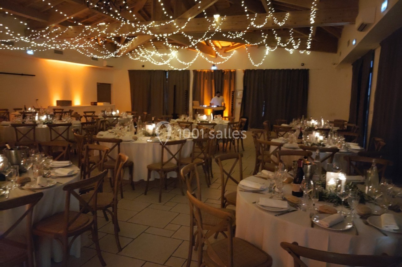 Salle de réception décorée avec des guirlandes lumineuses, tables rondes dressées et ambiance chaleureuse.