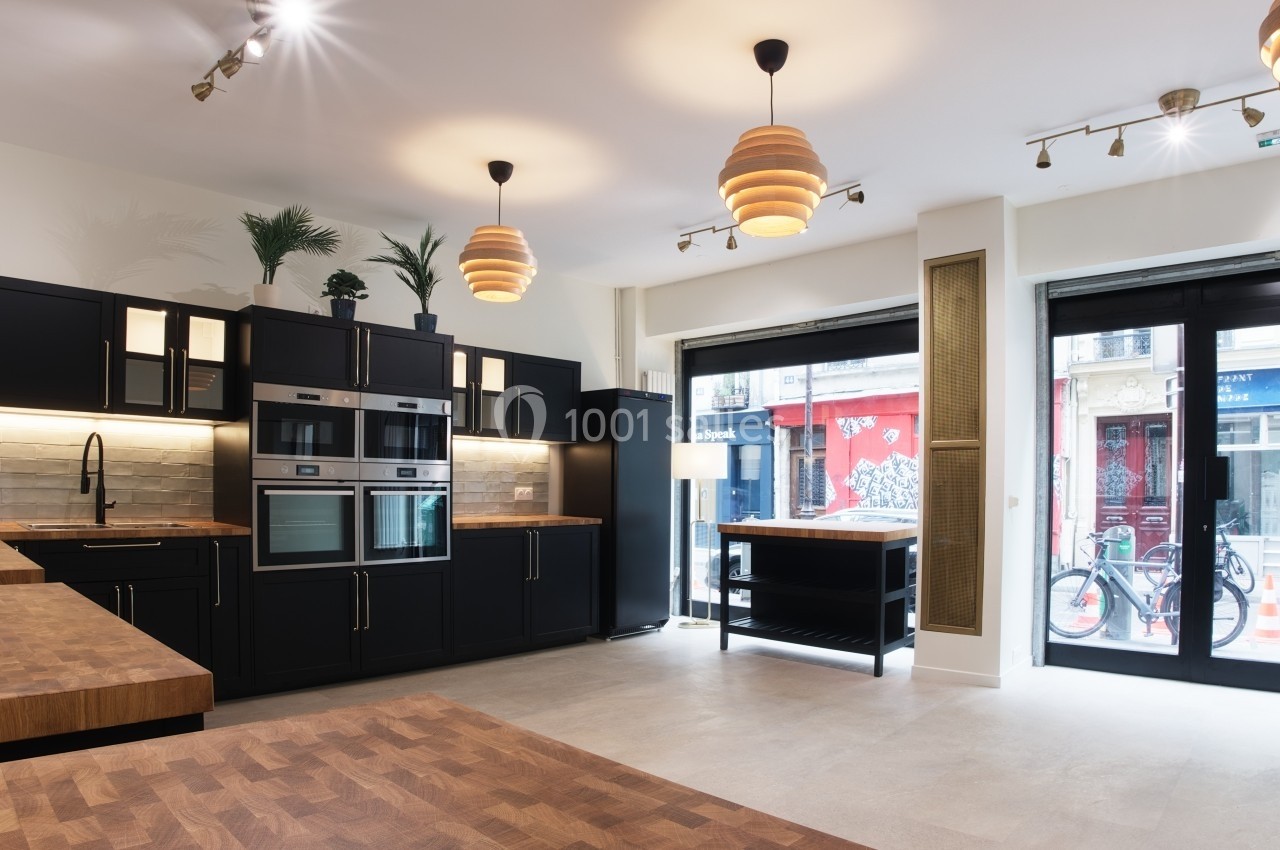 Cuisine moderne avec meubles noirs, plan de travail en bois, électroménagers intégrés et grande baie vitrée donnant sur la…