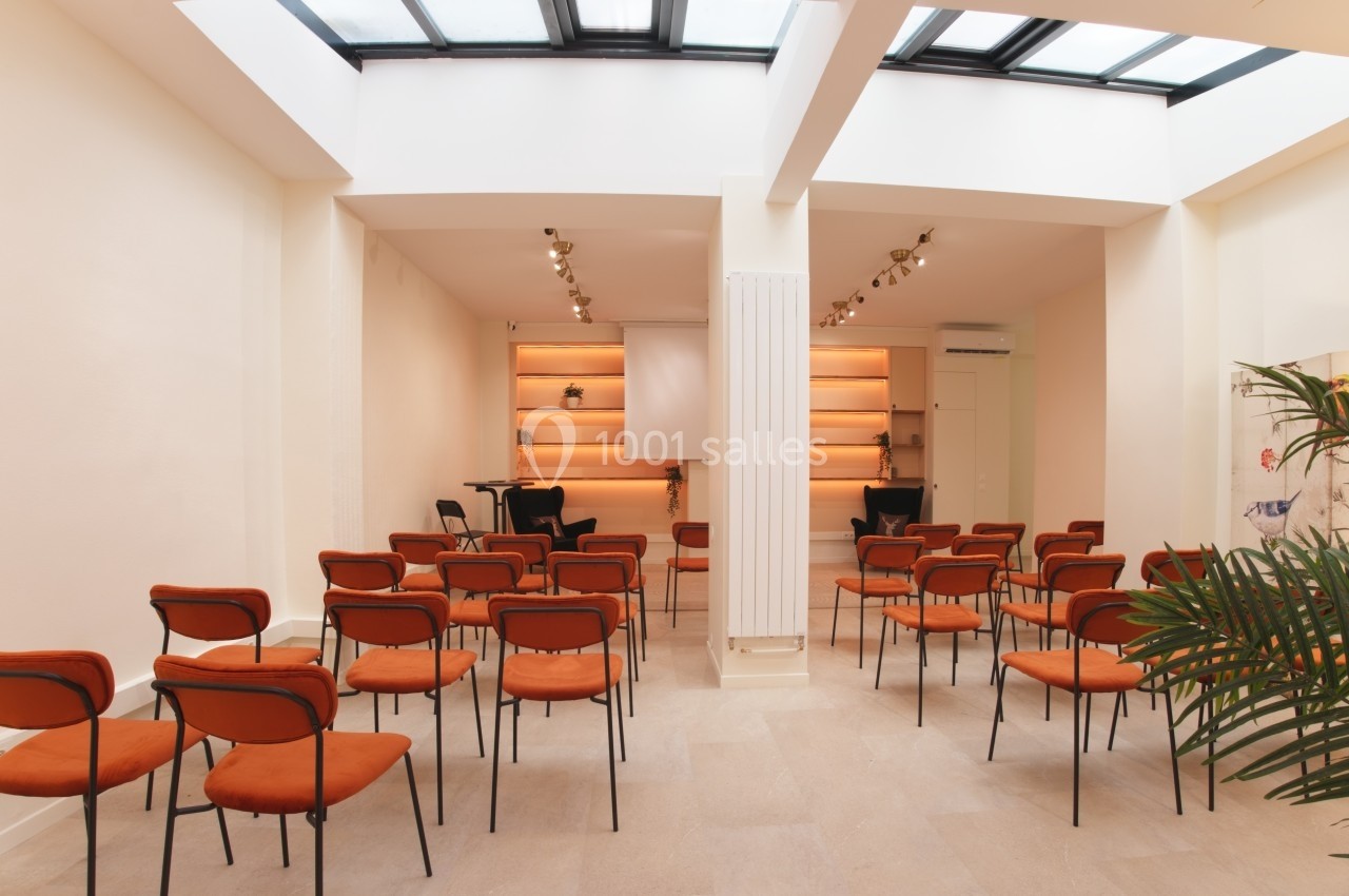 Salle lumineuse avec des chaises orange alignées, un écran de projection et des étagères éclairées en arrière-plan.