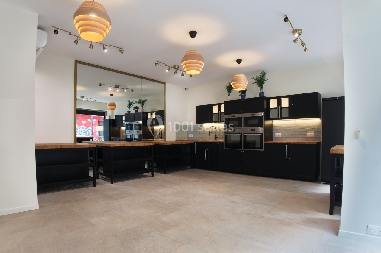 Cuisine moderne avec meubles noirs, plan de travail en bois, éclairage suspendu et grand miroir mural.