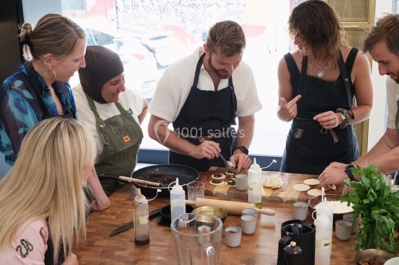 Un groupe de personnes en tabliers prépare des plats ensemble sur un plan de travail en bois.