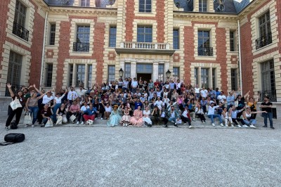 Des personnes tiennent un parachute coloré avec des trous, utilisé pour une activité de groupe en extérieur sur une pelouse.