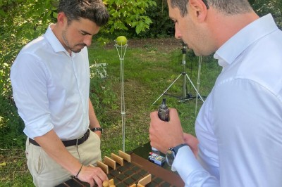 Des personnes tiennent un parachute coloré avec des trous, utilisé pour une activité de groupe en extérieur sur une pelouse.