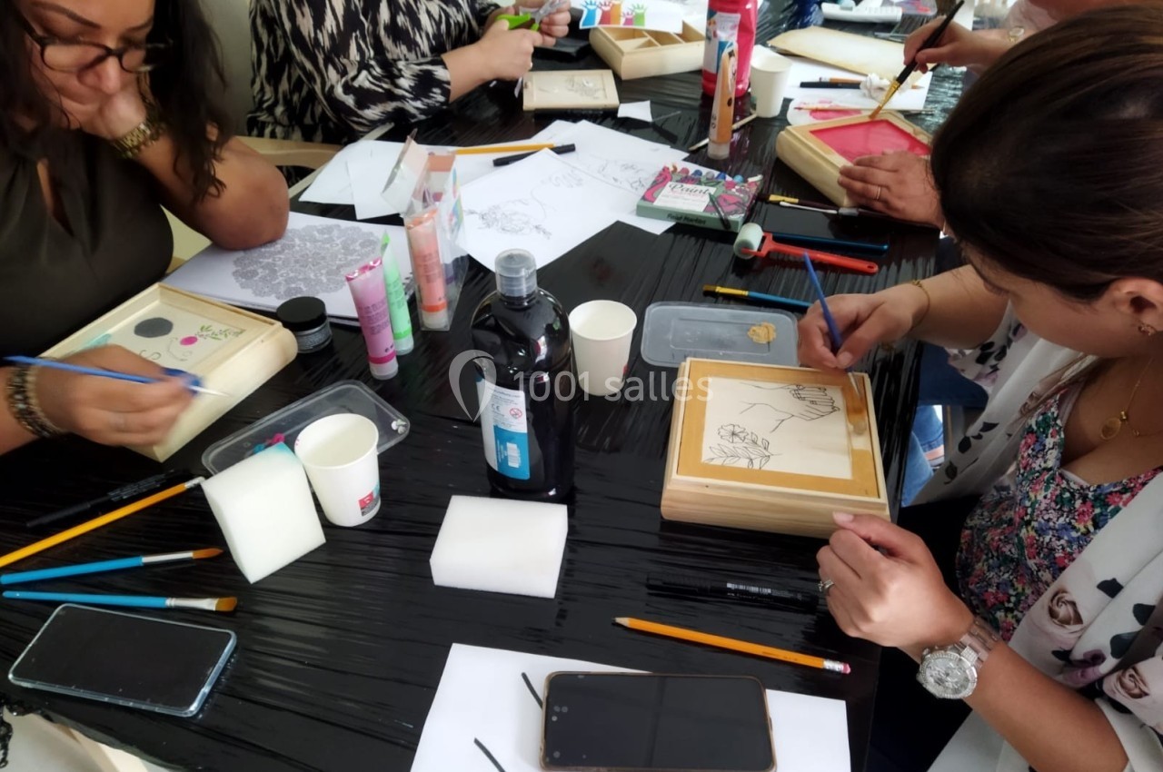 Des personnes participent à un atelier créatif, dessinant et peignant sur des supports en bois autour d'une table.