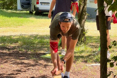 Des personnes tiennent un parachute coloré avec des trous, utilisé pour une activité de groupe en extérieur sur une pelouse.