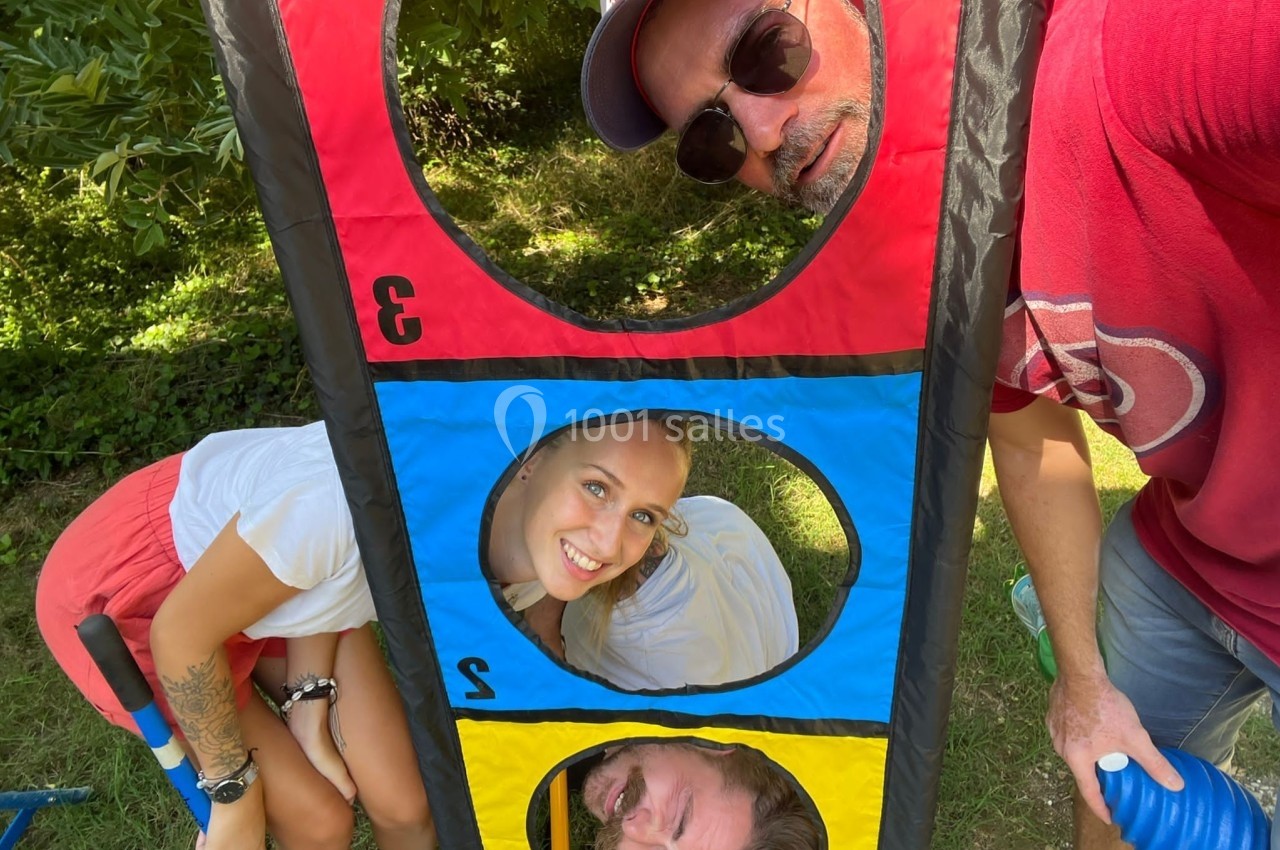 Trois personnes souriantes posant à travers les cercles colorés d'un jeu en plein air, dans un cadre verdoyant.