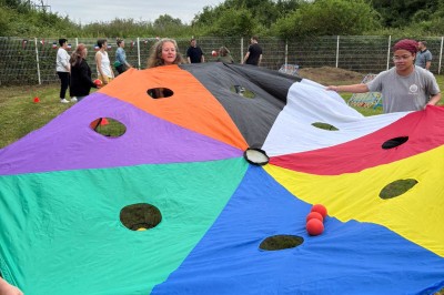 Des personnes tiennent un parachute coloré avec des trous, utilisé pour une activité de groupe en extérieur sur une pelouse.