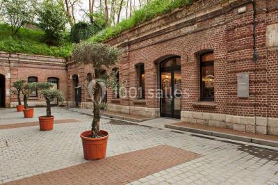 Espace extérieur aménagé pour un événement avec tables hautes, buffet et tente blanche, entouré de verdure.