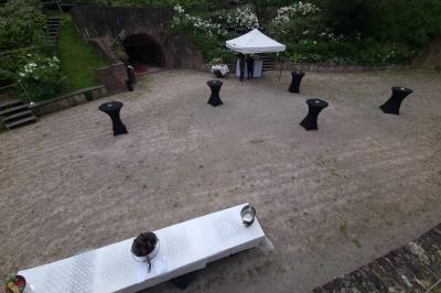 Espace extérieur aménagé pour un événement avec tables hautes, buffet et tente blanche, entouré de verdure.