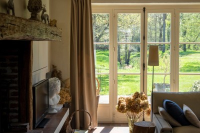 Paysage verdoyant avec arbres feuillus, pelouse ensoleillée et petit pont en pierre près d'un ruisseau.