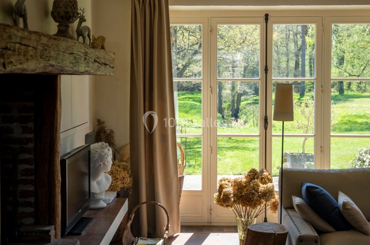 Salon lumineux avec une grande baie vitrée donnant sur un jardin verdoyant, décoré de fleurs séchées et d'éléments naturels.