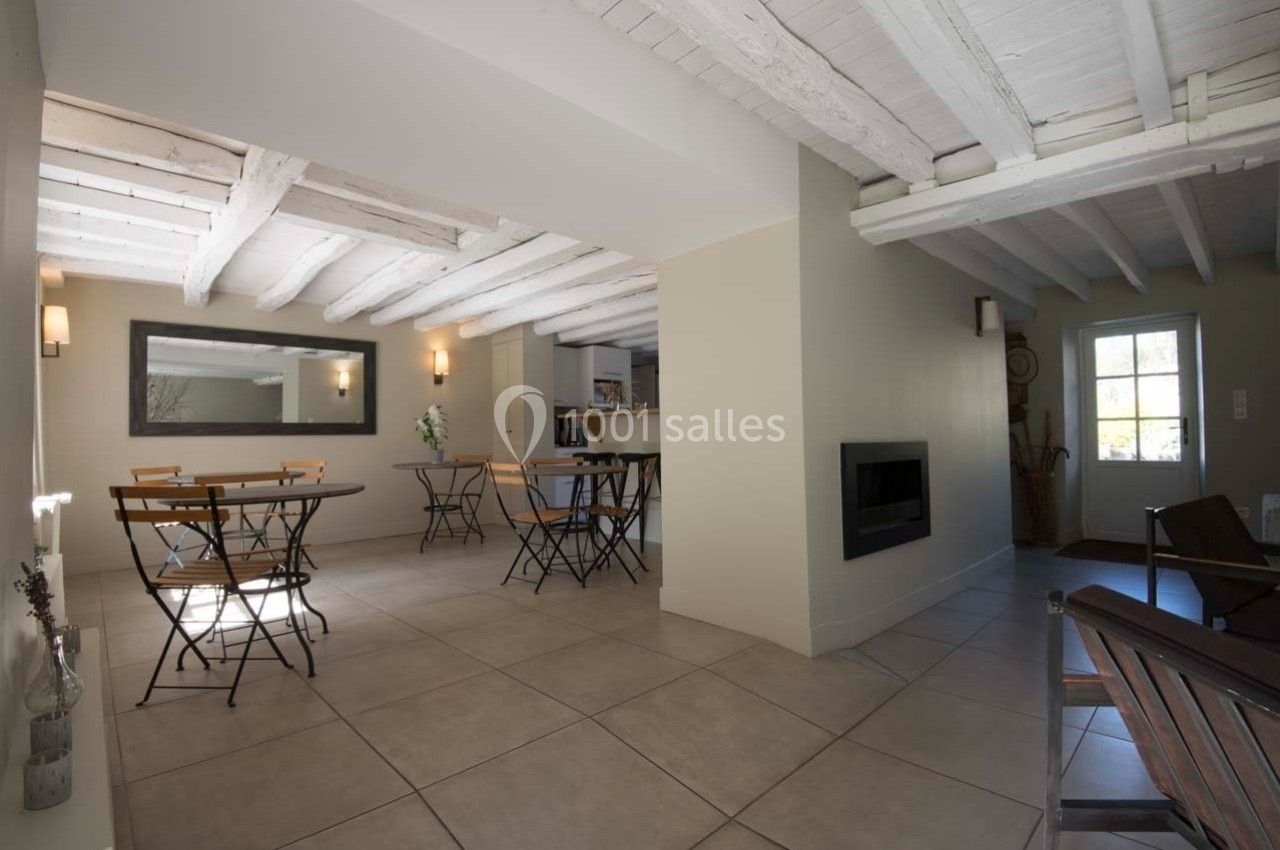 Salle lumineuse avec tables et chaises en métal, plafond en poutres blanches et porte vitrée donnant sur l'extérieur.