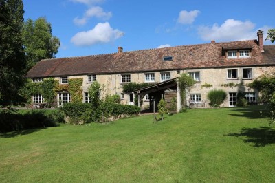 Paysage verdoyant avec arbres feuillus, pelouse ensoleillée et petit pont en pierre près d'un ruisseau.