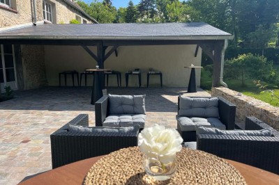 Paysage verdoyant avec arbres feuillus, pelouse ensoleillée et petit pont en pierre près d'un ruisseau.