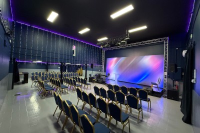 Groupe de personnes rassemblées dans une salle sombre avec éclairage bleu, buffet et grand écran en arrière-plan.