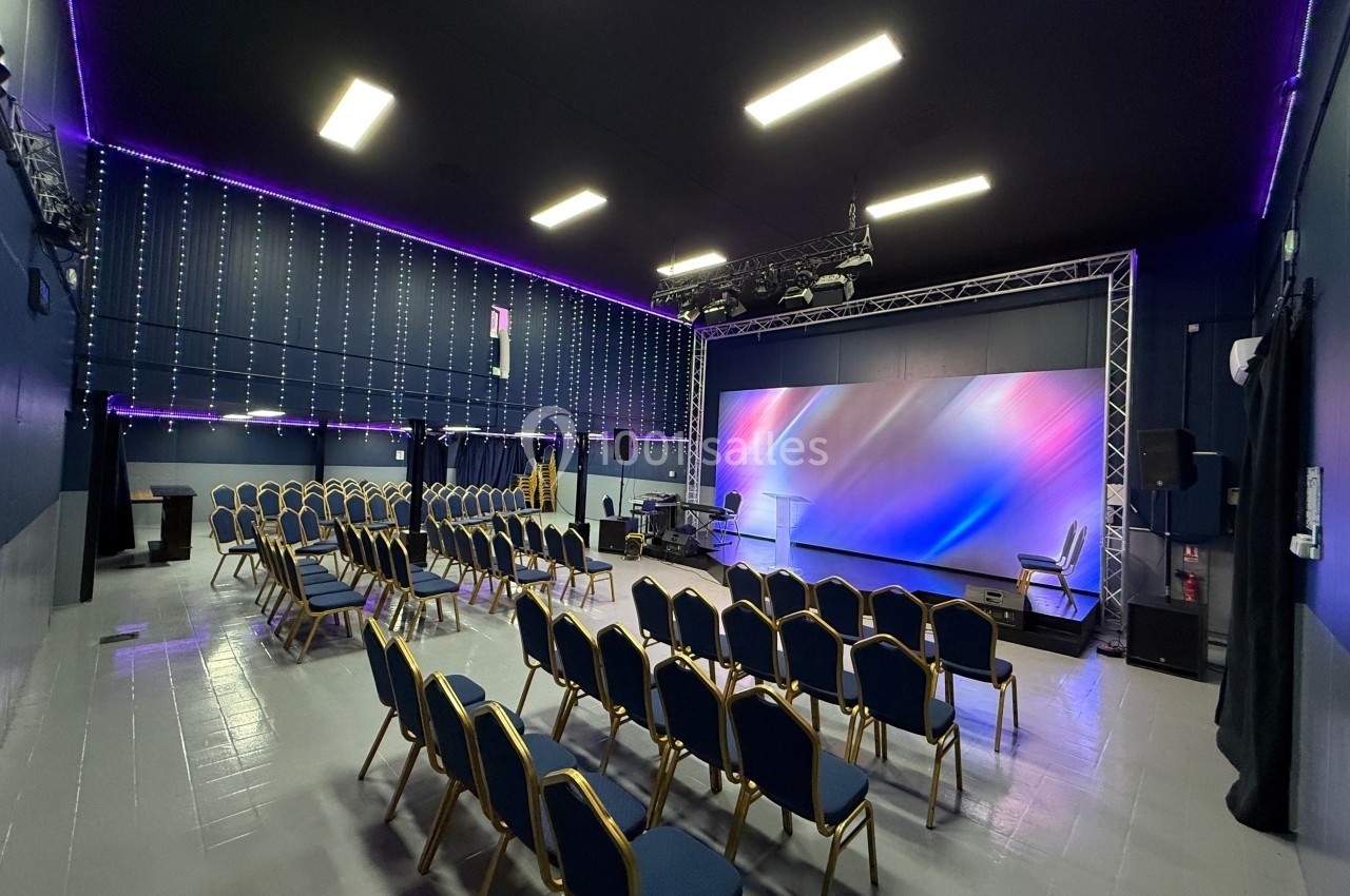 Salle de conférence moderne avec chaises alignées, scène équipée d'un écran lumineux et éclairage LED au plafond.
