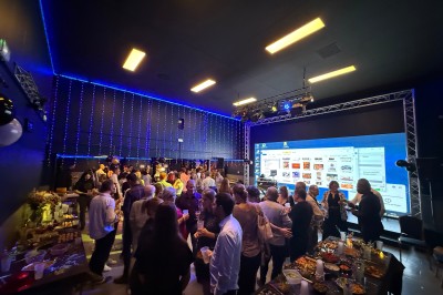 Groupe de personnes rassemblées dans une salle sombre avec éclairage bleu, buffet et grand écran en arrière-plan.