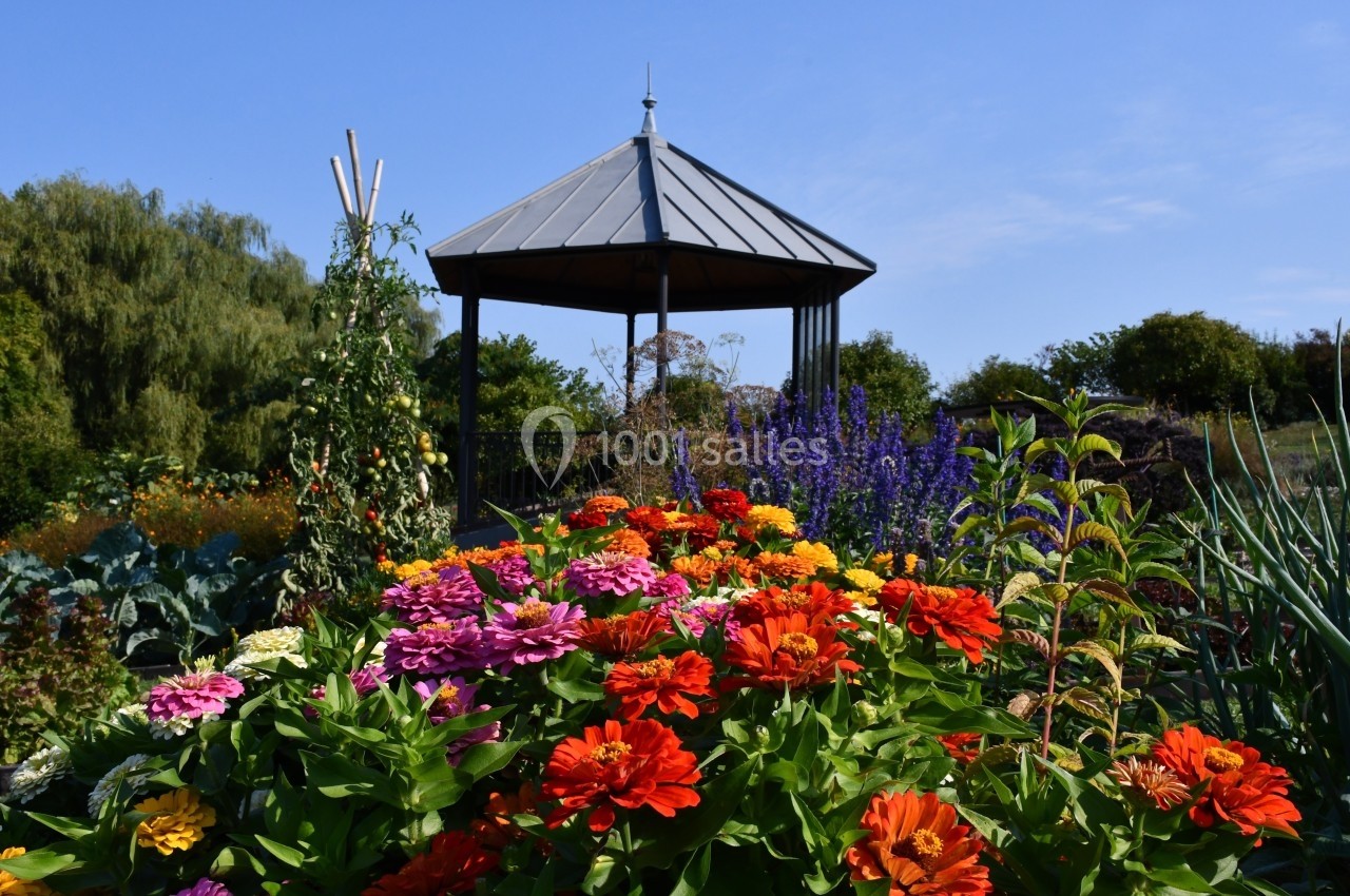 Massif de fleurs colorées devant un kiosque en métal noir, entouré de végétation sous un ciel bleu.